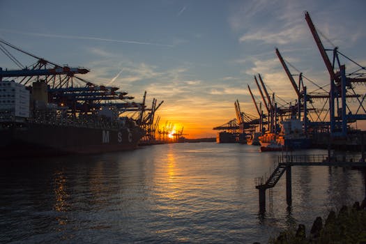 Shipping vessels at Hamburg port during a vibrant sunset, showcasing industrial cranes.